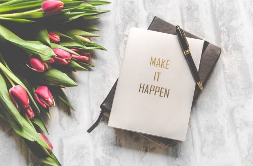 A notebook with 'Make It Happen' inscription beside a bouquet of pink tulips, capturing inspiration.